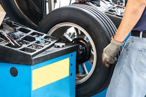 Person balancing a tire on a blue machine in a repair shop.