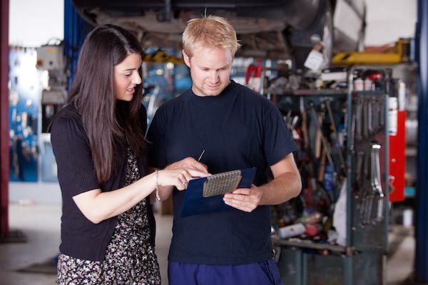 Woman points to document held by mechanic in auto repair shop.