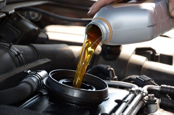 Pouring oil from a silver bottle into a car engine.