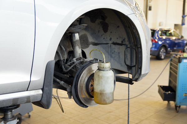 Car wheel in repair shop with fluid collection bottle attached for brake bleeding.