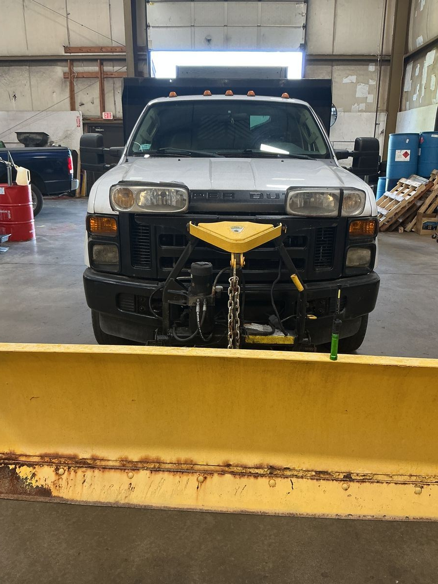 White pickup truck with yellow snowplow attached, parked in a garage. | Accomplished Automotive