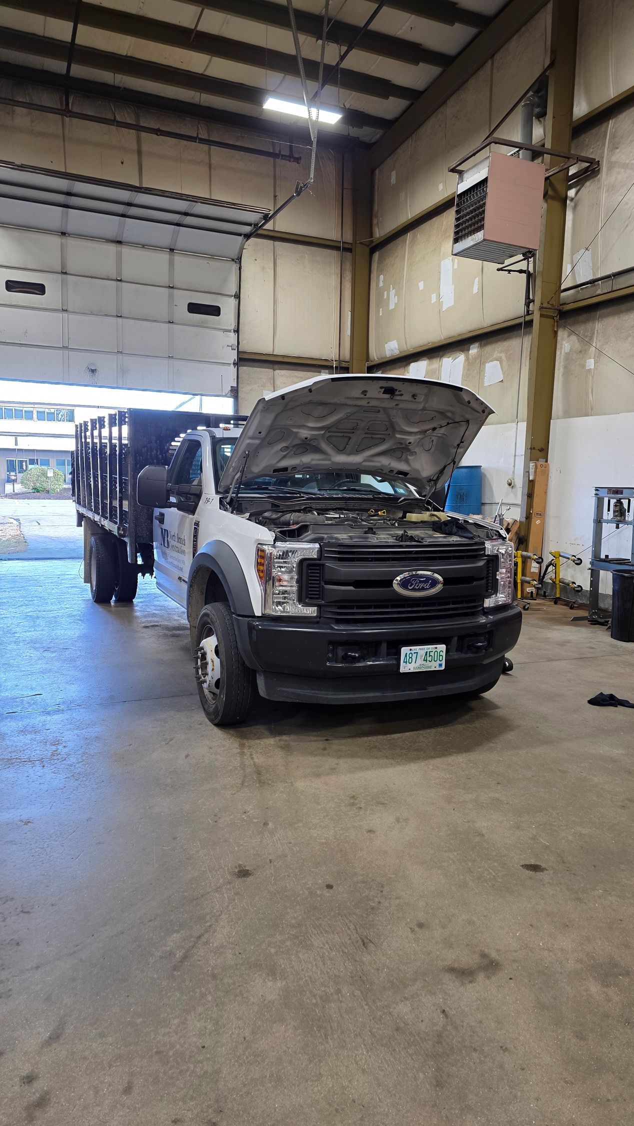 Truck with open hood inside a garage, next to a closed bay door. | Accomplished Automotive