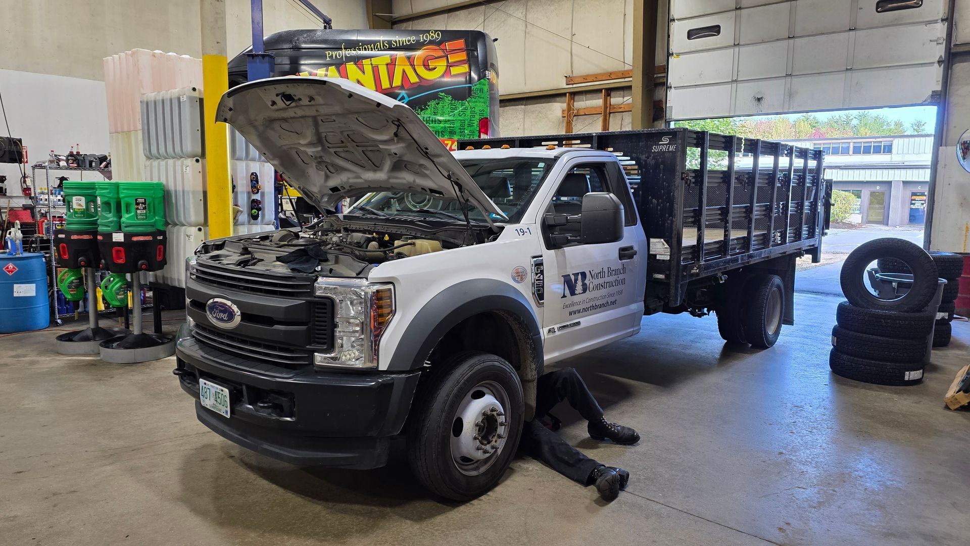 White truck with bed and open hood; person working on the front in a repair shop. | Accomplished Automotive