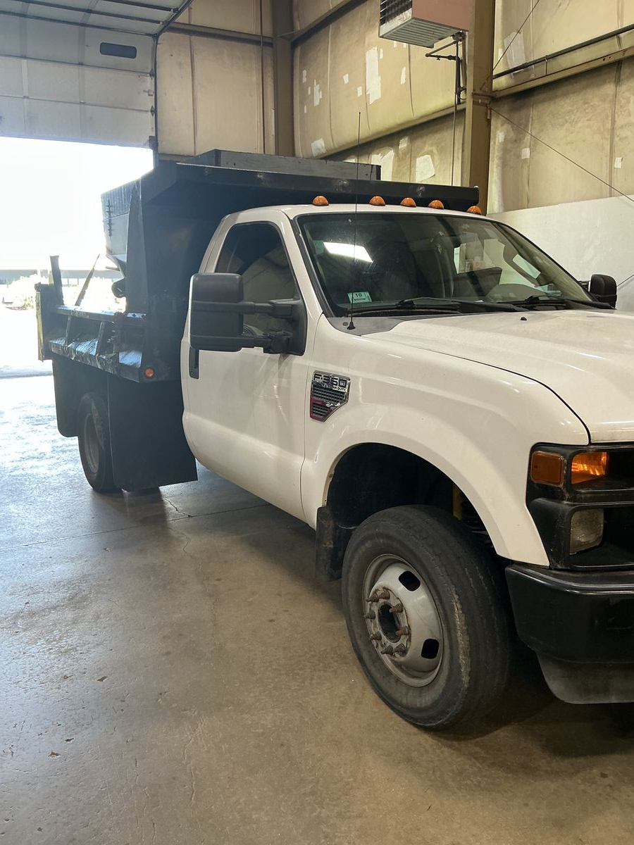 White Ford F-350 dump truck parked inside a warehouse. Black dump bed. | Accomplished Automotive