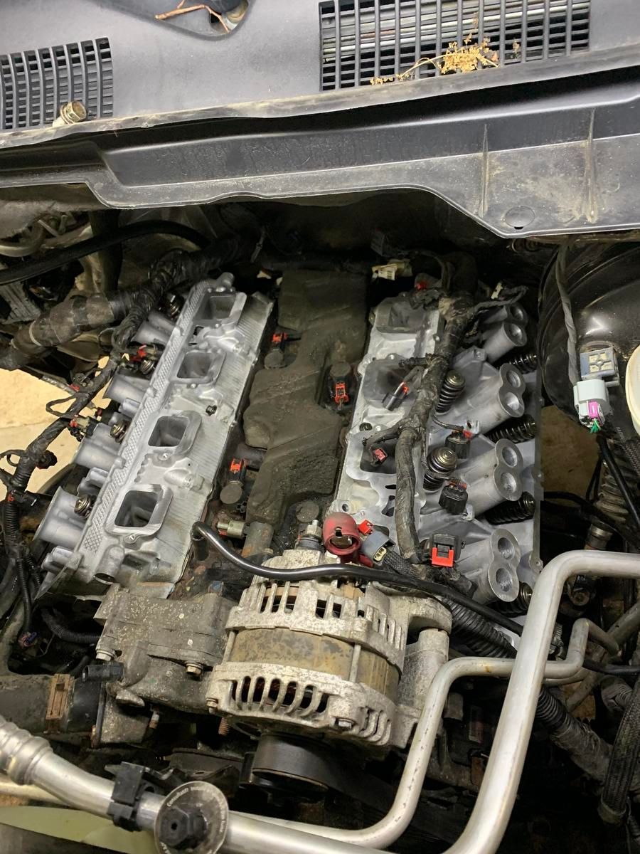 Engine compartment of a vehicle, partially disassembled. Visible are the engine heads, fuel injectors, and alternator. | Accomplished Automotive