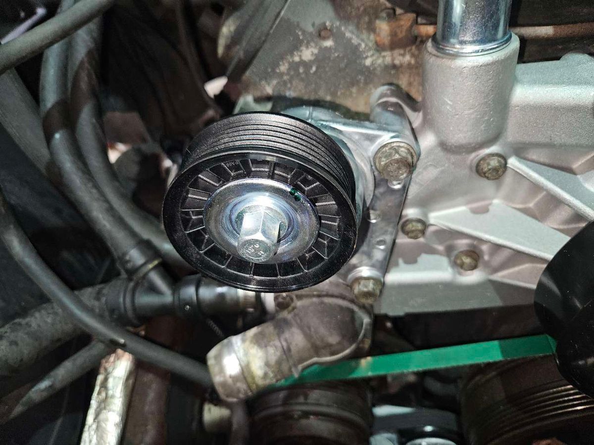 Black pulley on an engine. Close up of the belt tensioner, bolts and hoses. | Accomplished Automotive