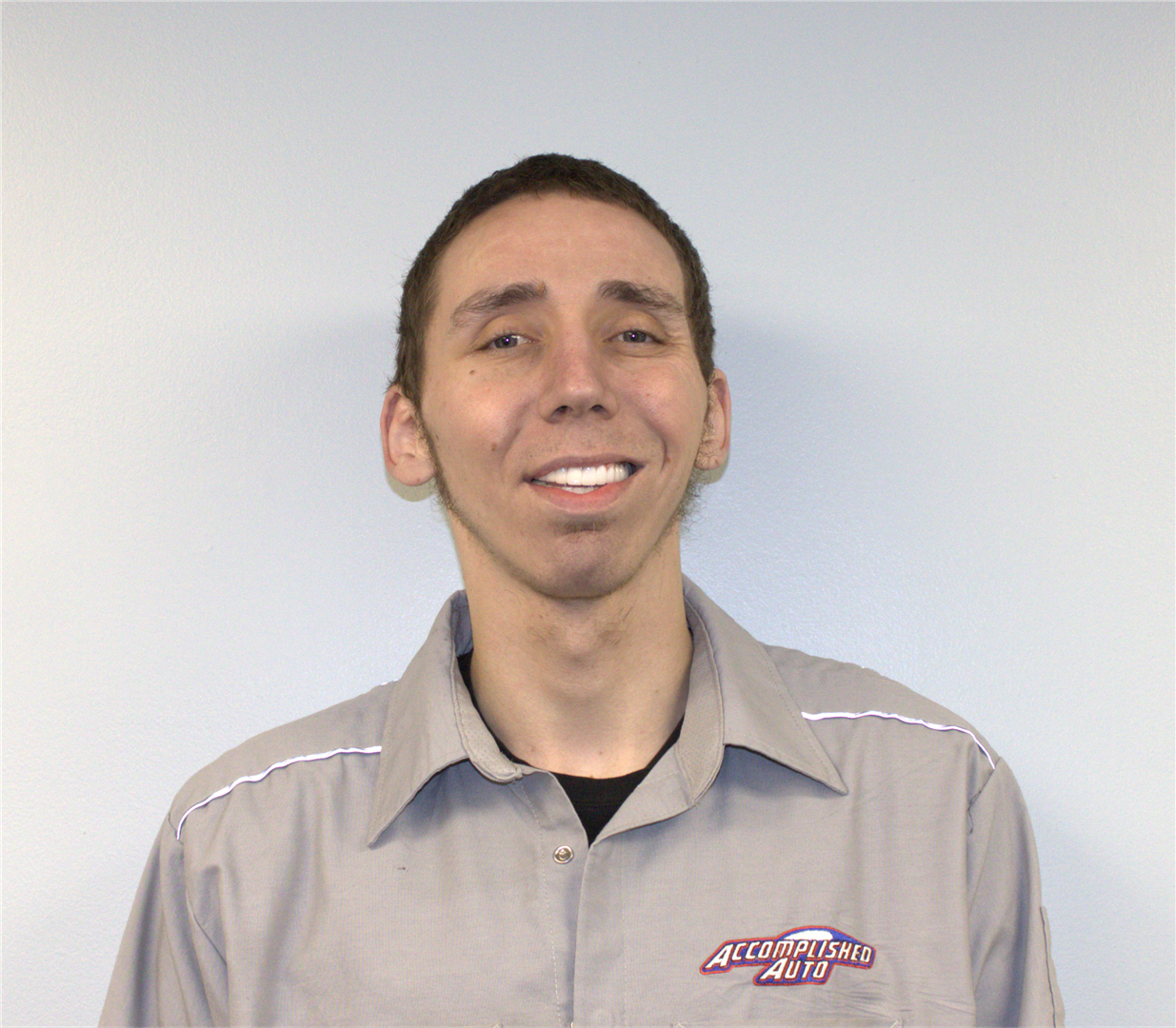 Man in gray uniform smiling at the camera, with a logo on the shirt, against a white backdrop.