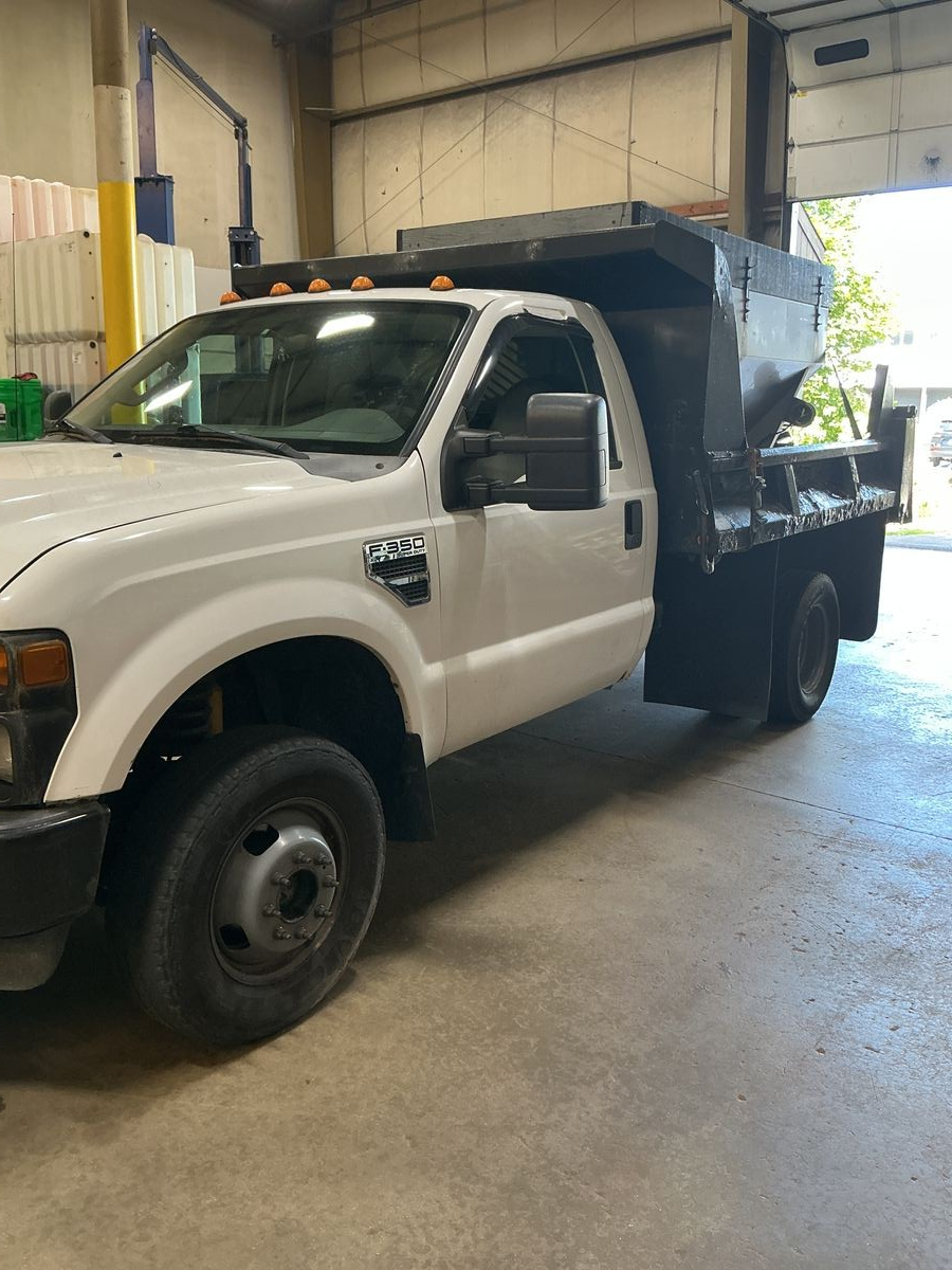 White Ford F-350 dump truck parked in a garage. Black dump bed, grey wheels, and a partly open door. | Accomplished Automotive