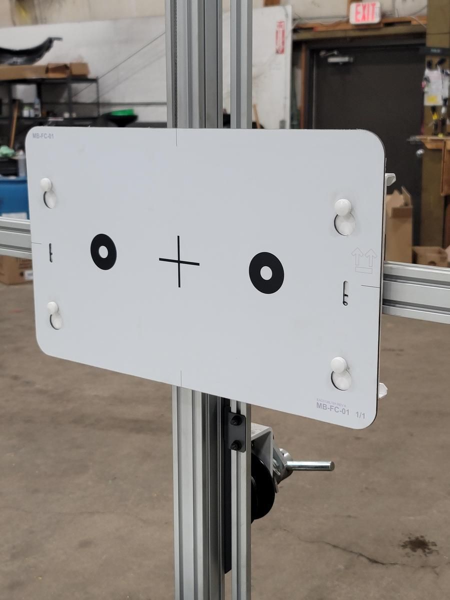White calibration target with black circles and crosshairs, mounted on a metal pole in a workshop. | Accomplished Automotive