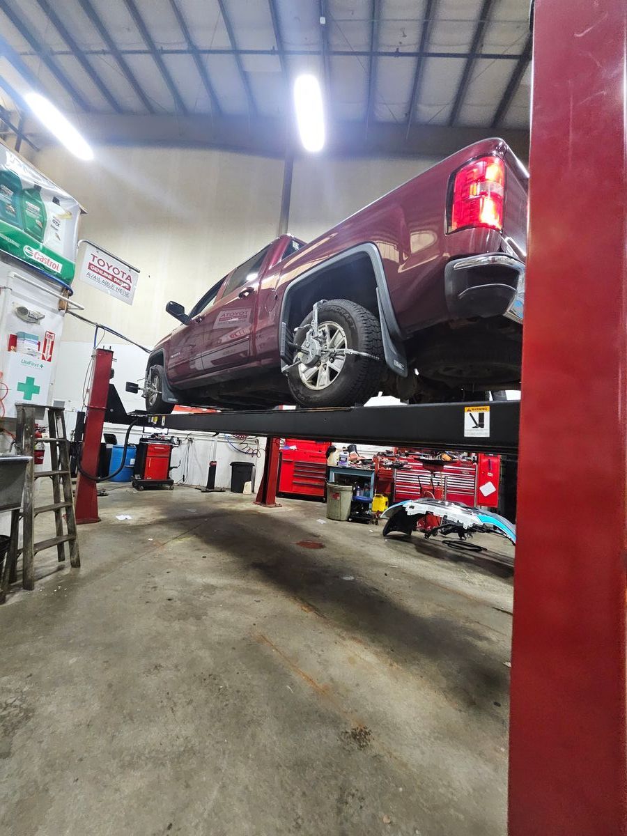 A maroon pickup truck raised on a hydraulic lift in a repair shop. | Accomplished Automotive