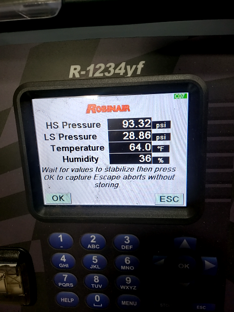 A Robinair R-1234yf AC machine display showing high-side and low-side pressures, temperature, and humidity readings.