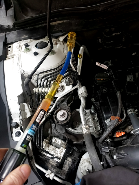 Engine bay with a gauge connected to an AC system for maintenance.