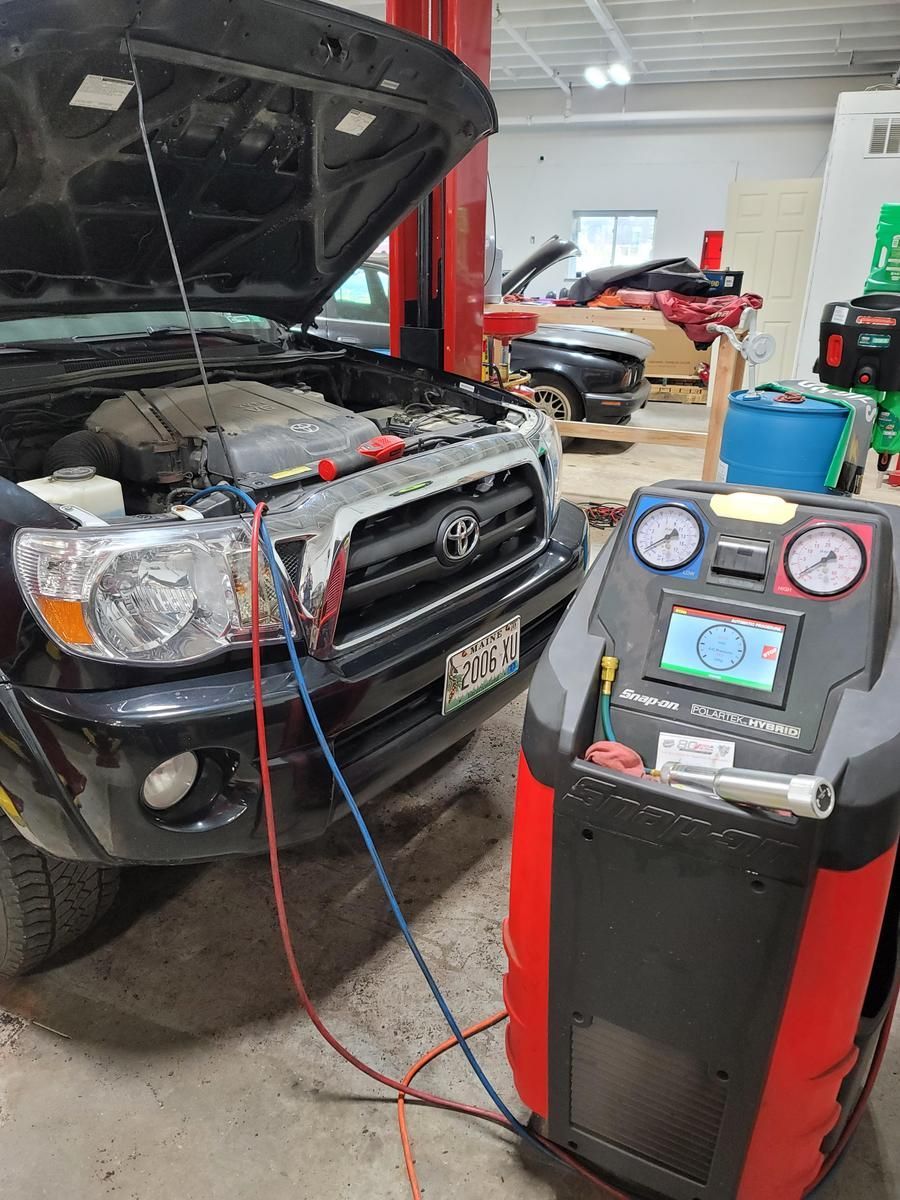 A black truck with its hood open being serviced by an AC machine. Red and blue hoses are attached. | Accomplished Automotive