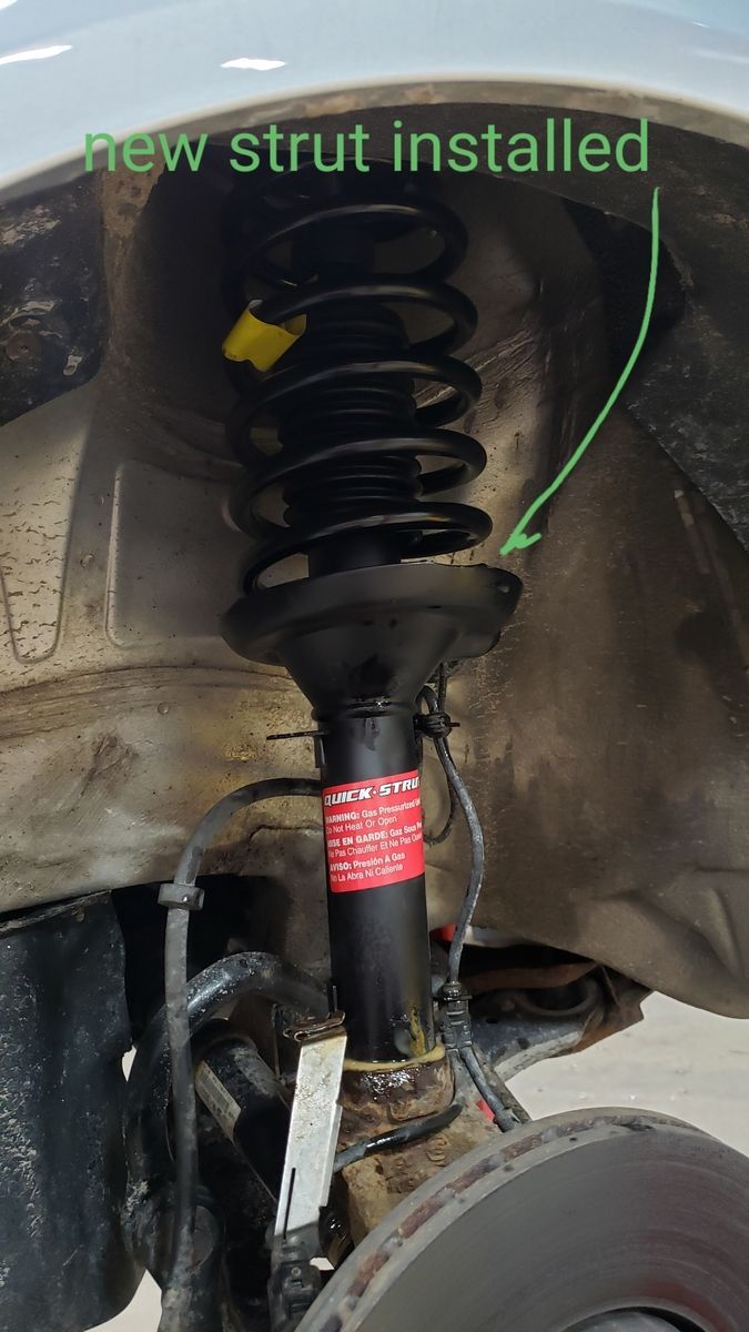 New black car strut with coil spring in wheel well, installed on a vehicle. | Accomplished Automotive