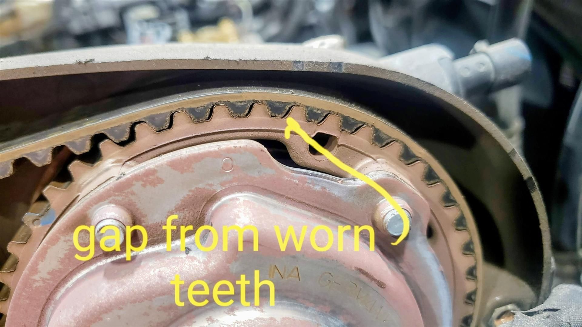 Close-up of a worn timing belt on an engine. A visible gap exists between the belt's teeth and the gear.