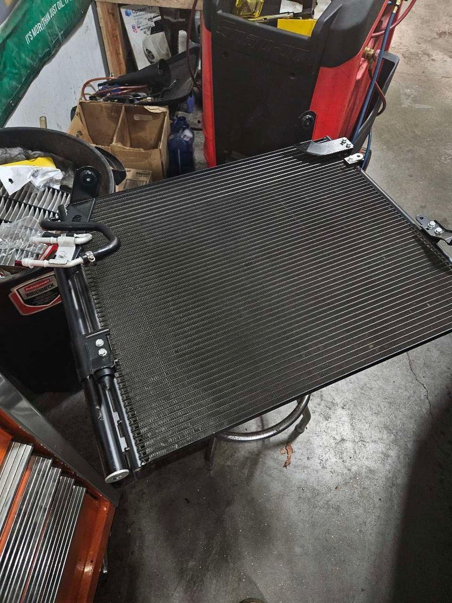 Black automotive radiator with tools attached, resting on a stool in a garage. | Accomplished Automotive