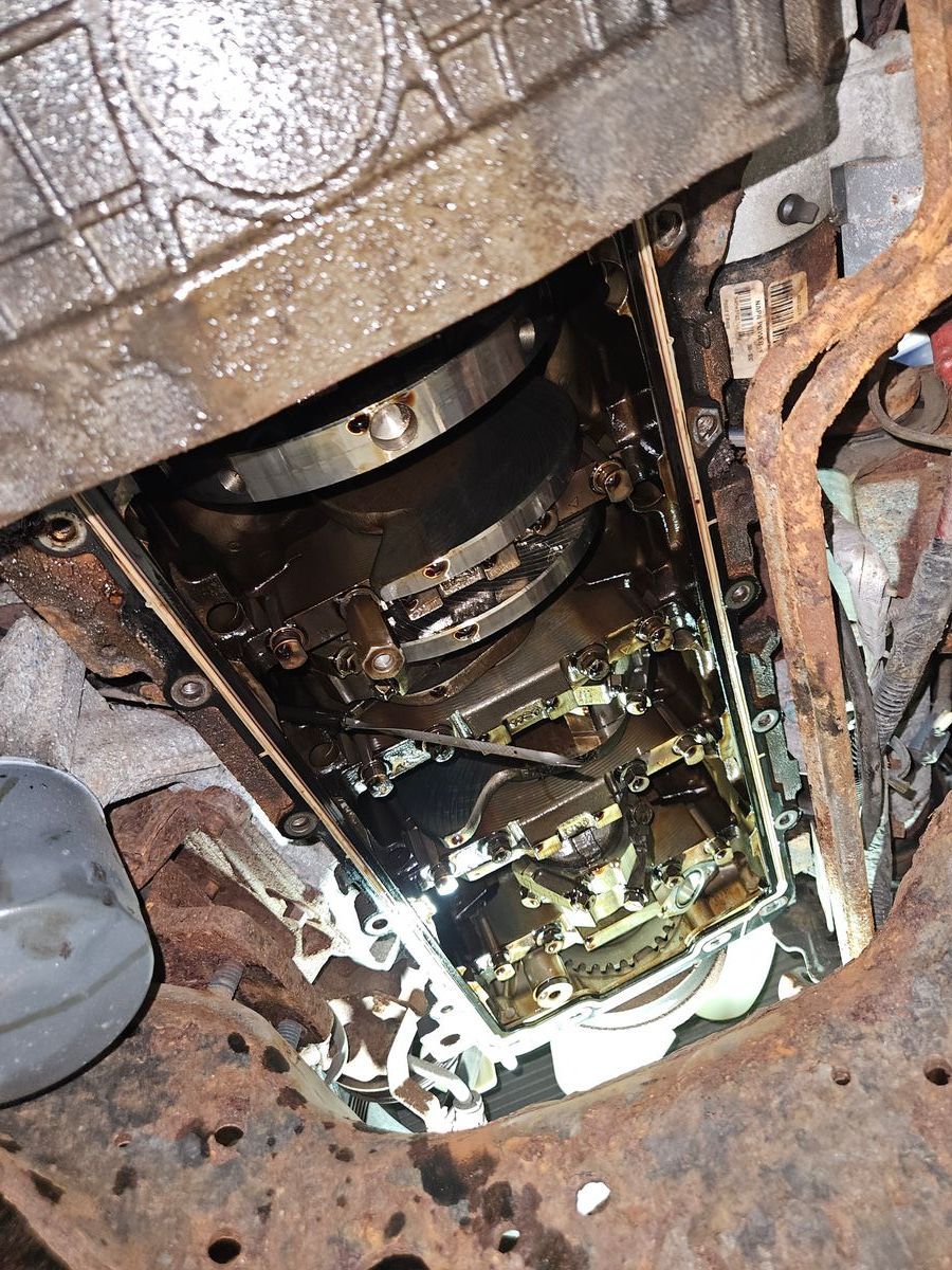 Engine's oil pan removed, revealing engine internals, bearings, and oil-covered components within the vehicle's undercarriage. | Accomplished Automotive