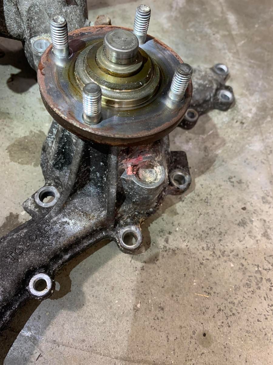 Close-up of a rusty car axle with a wheel hub attached, bolts visible. | Accomplished Automotive