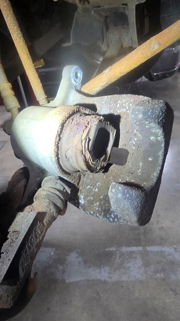 Corroded car brake caliper removed from a vehicle, showing wear and rust.