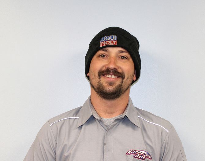 Man in a Liqui Moly beanie and mechanic shirt smiles, standing against a light background.