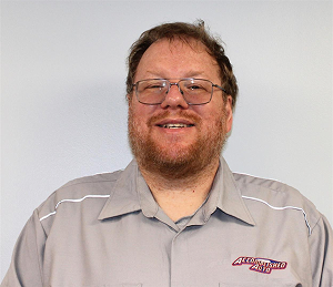 Man with glasses and a beard in a gray shirt with white trim smiles.