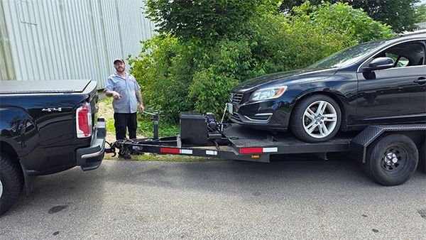 A black truck pulling a car trailer with a black car on it; a man stands near.