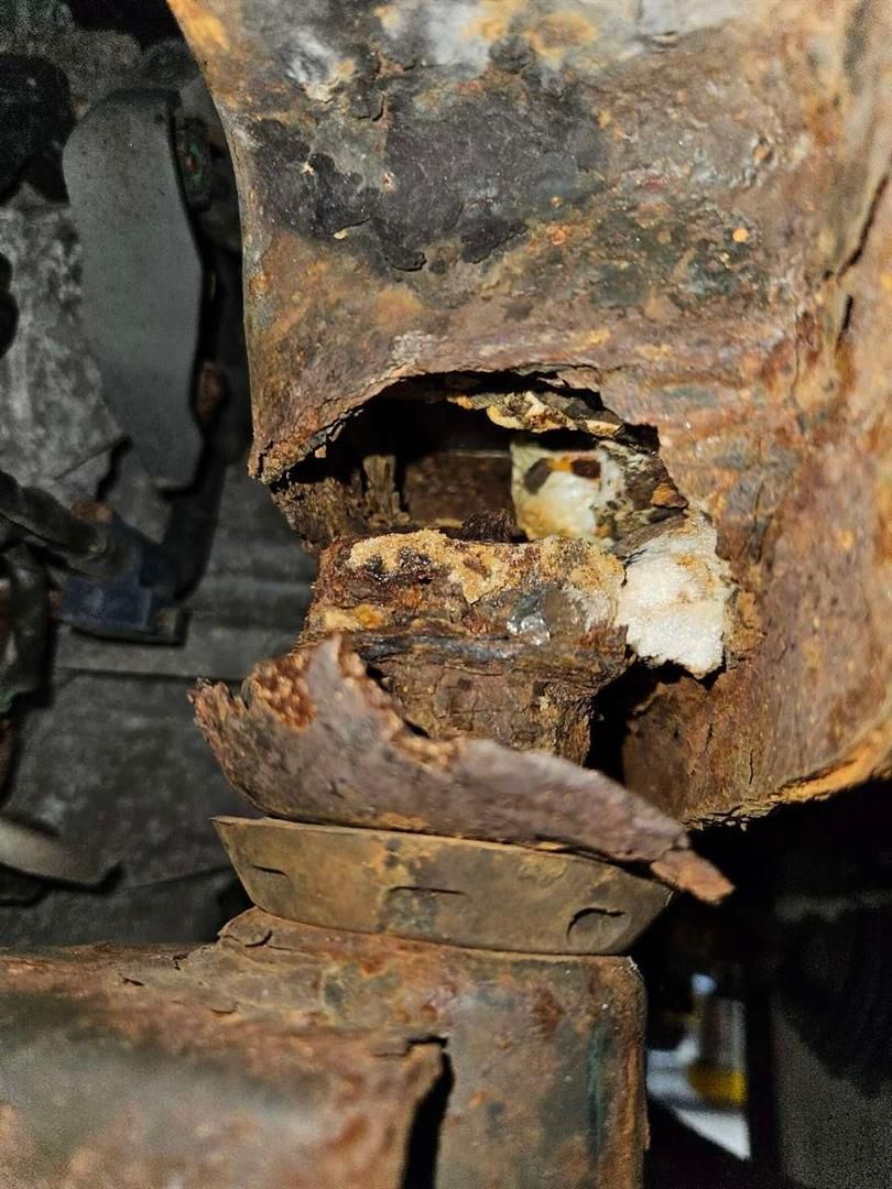 Severely rusted car suspension component with significant metal deterioration.