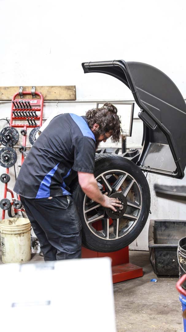 Mechanic balancing a car tire in a garage. Wearing blue and black uniform.