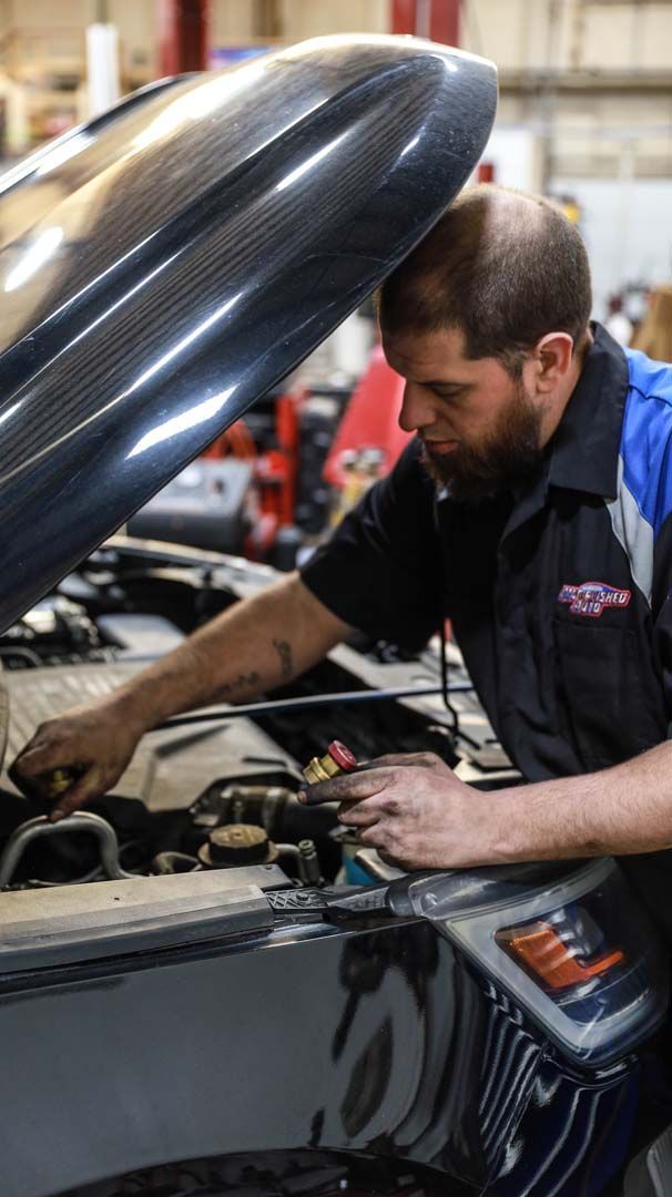 Mechanic working on a car engine in a garage. He leans over the hood, inspecting components.