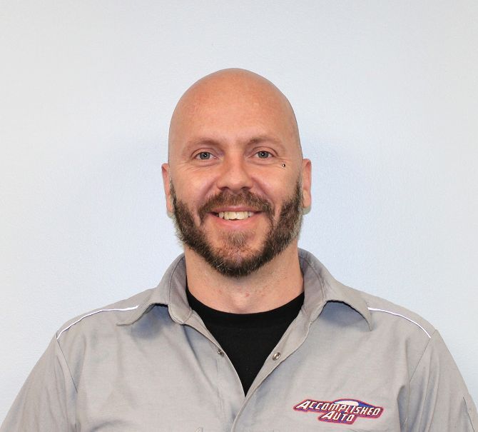 Bald man with a beard smiles, wearing a gray work shirt with