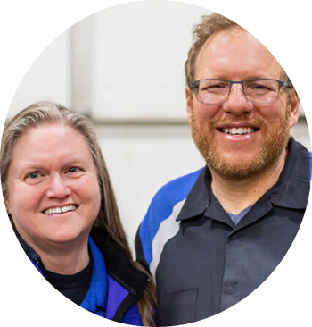 Two people smiling at the camera, indoors. The man wears glasses and a blue uniform. | Accomplished Auto