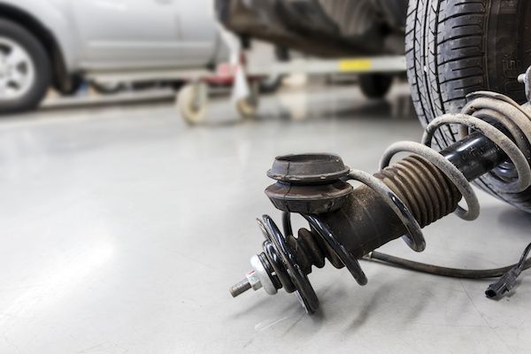 Car suspension system with a spring, shock, and tire, on a garage floor.