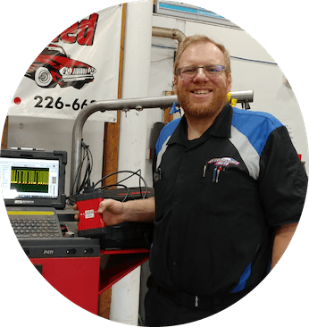 Mechanic smiling, holding diagnostic tool. Standing in garage with car equipment.