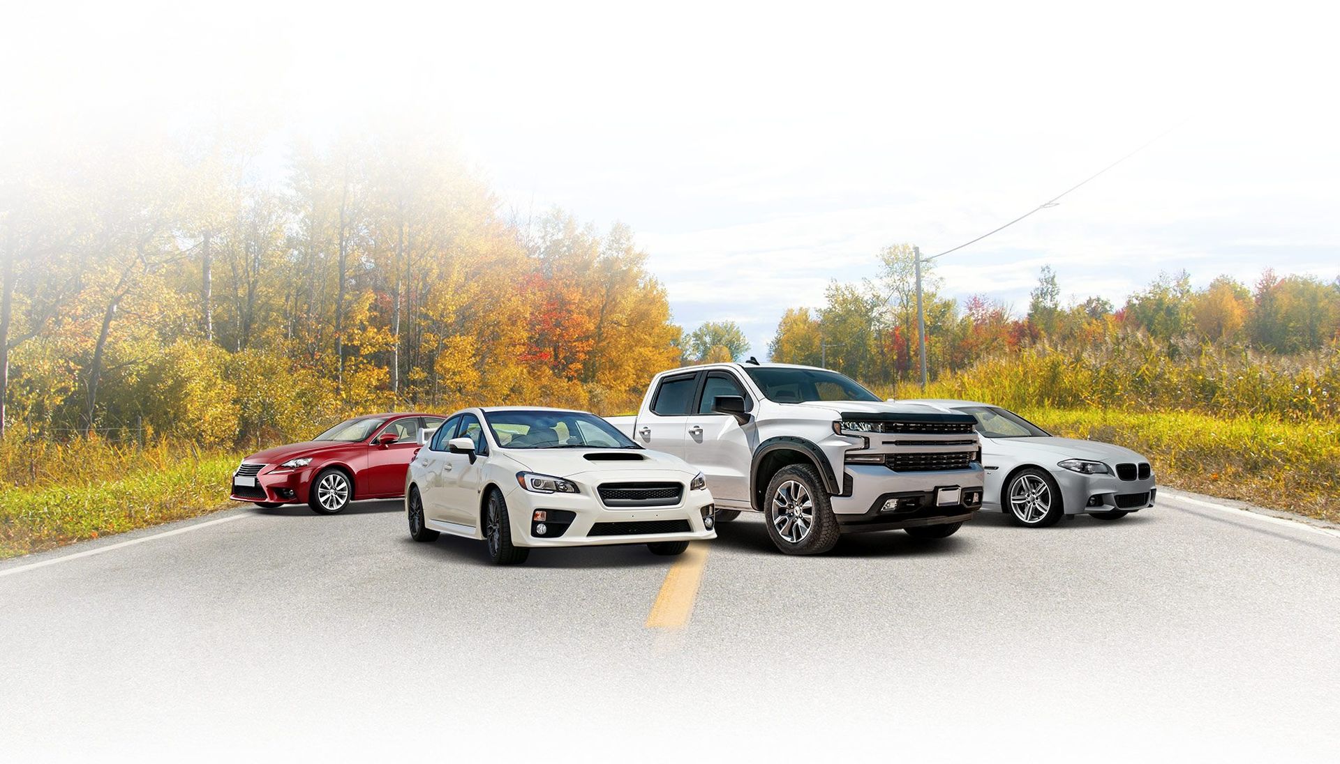 Cars on a road with autumn foliage in the background. Includes red, white, silver, and a white pickup truck.