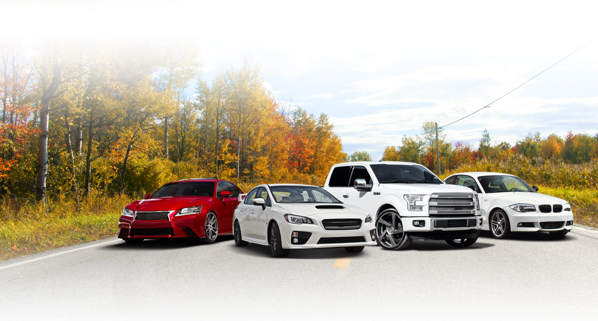 Cars on a road with autumn foliage in the background. Includes red, white, silver, and a white pickup truck.