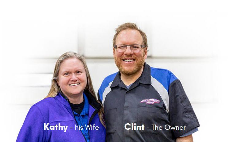 Two people, Kathy and Clint, smiling in front of a white background. Kathy is wearing a purple jacket, and Clint is in a blue and black mechanic shirt.