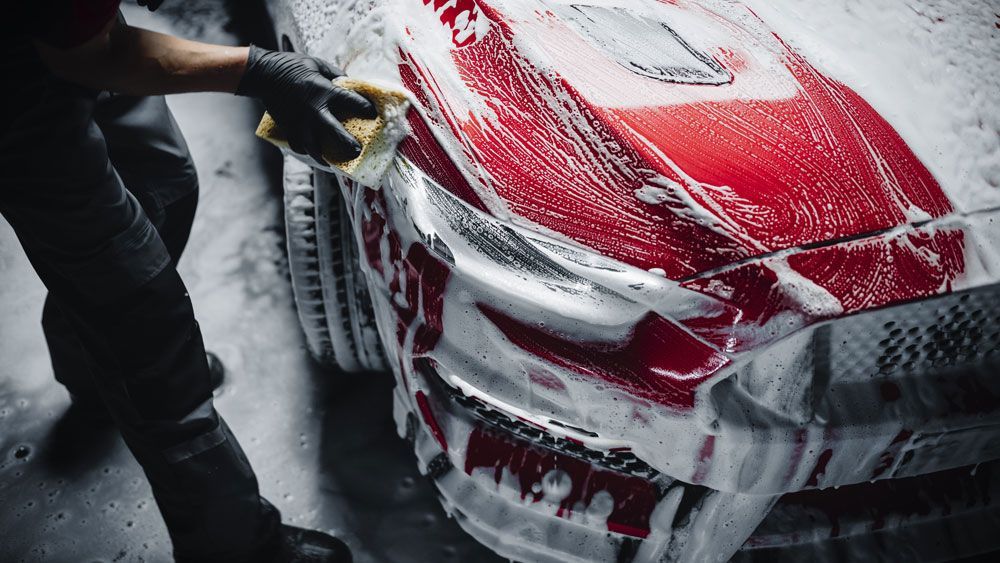 A man is washing a red car with foam and a cloth.