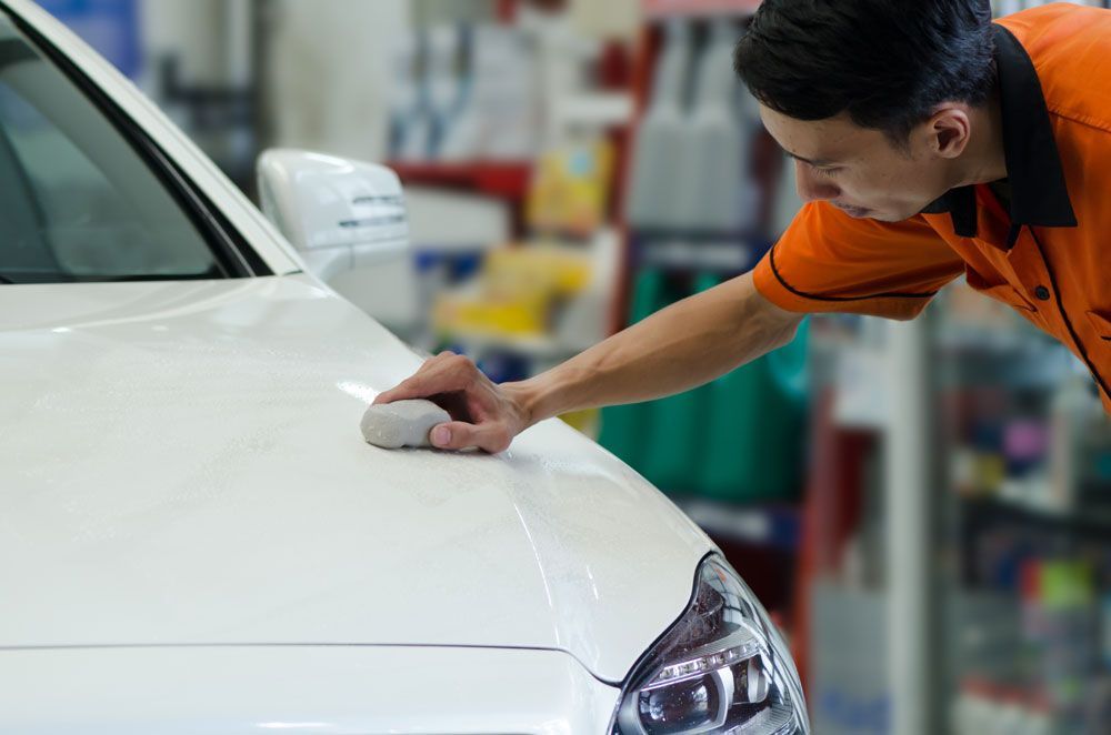 A man is polishing the hood of a white car.