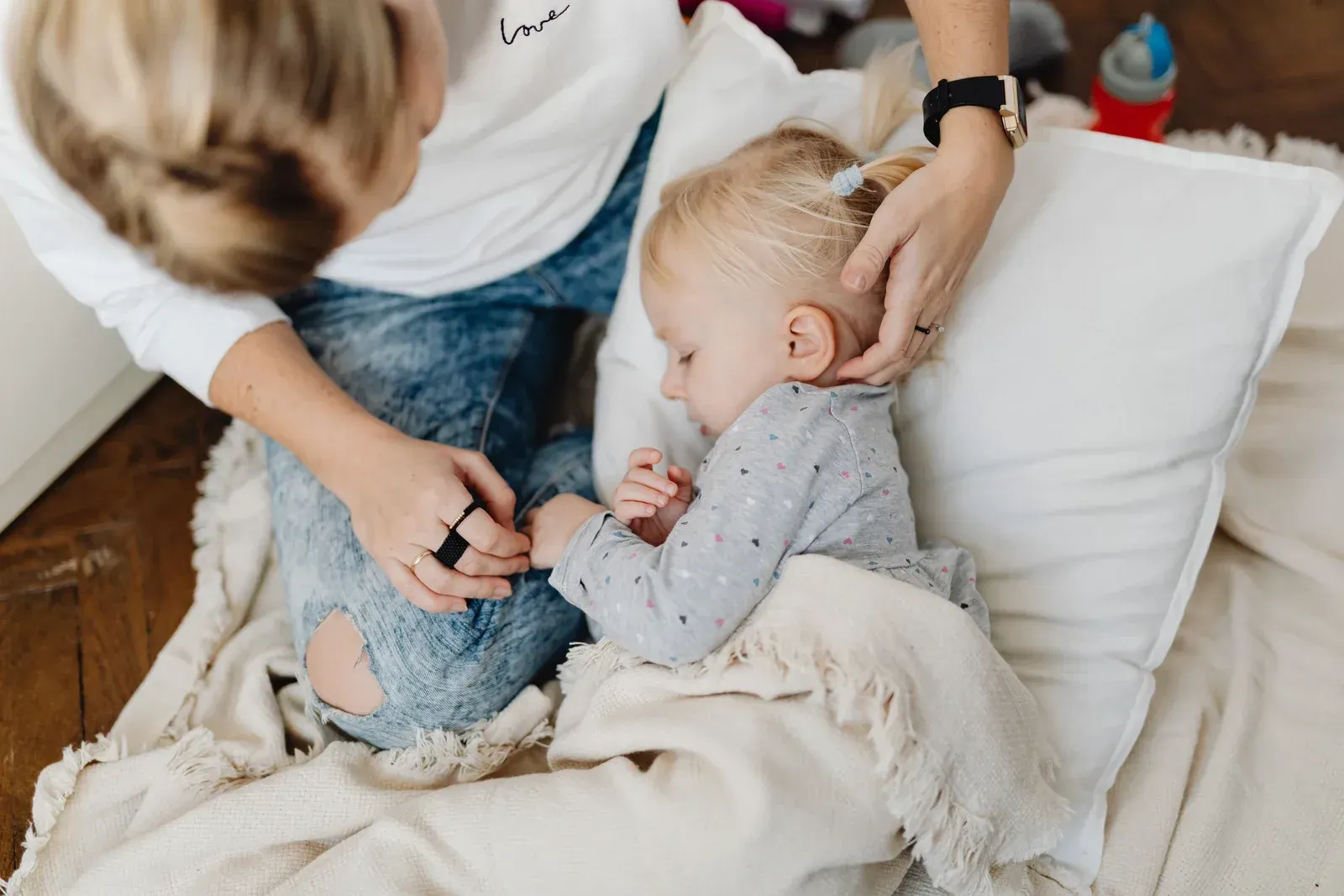 Person comforting a sleeping child on a pillow and blanket.