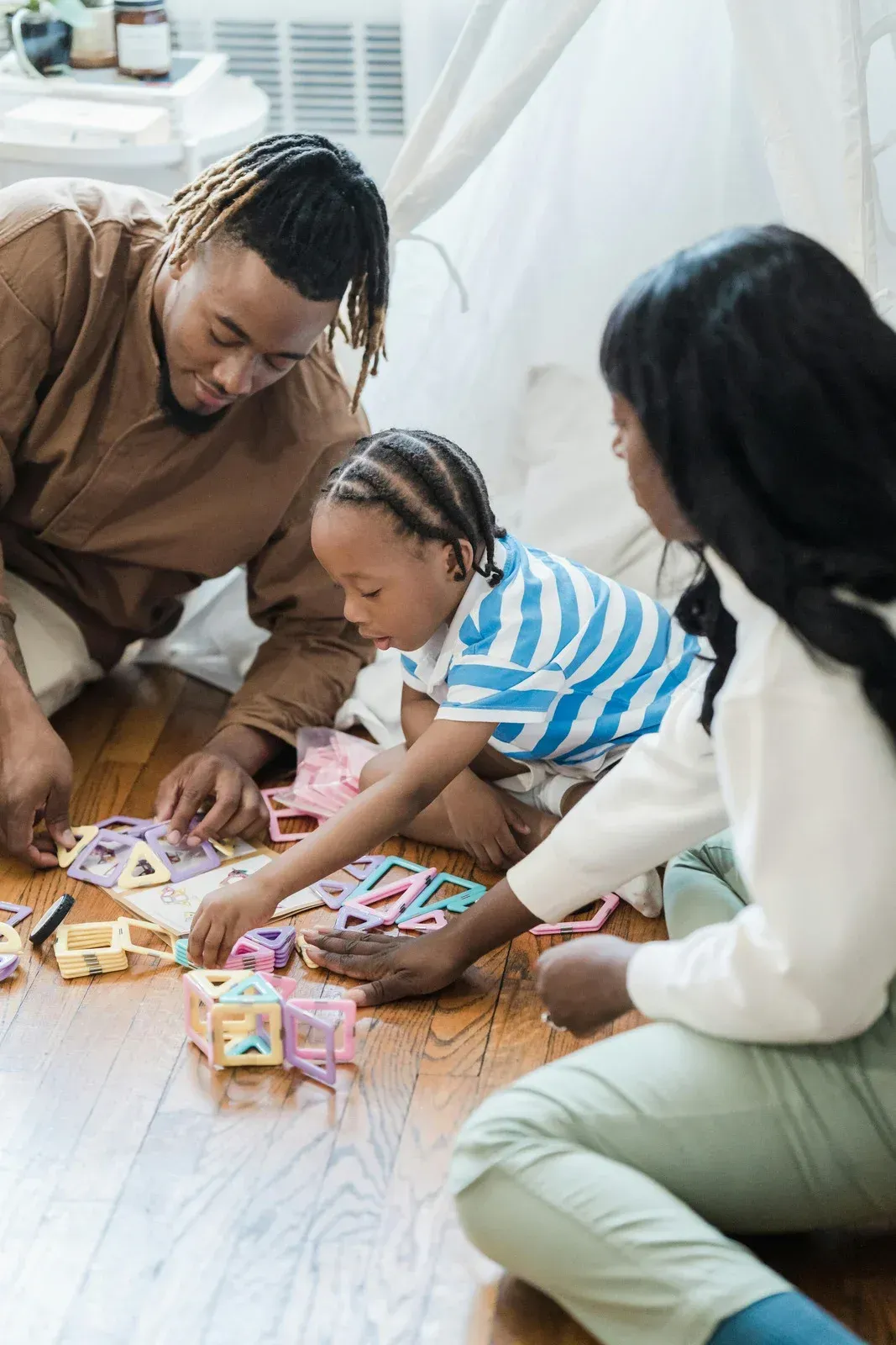 Family playing with colorful blocks on a wooden floor in front of a white tent.
