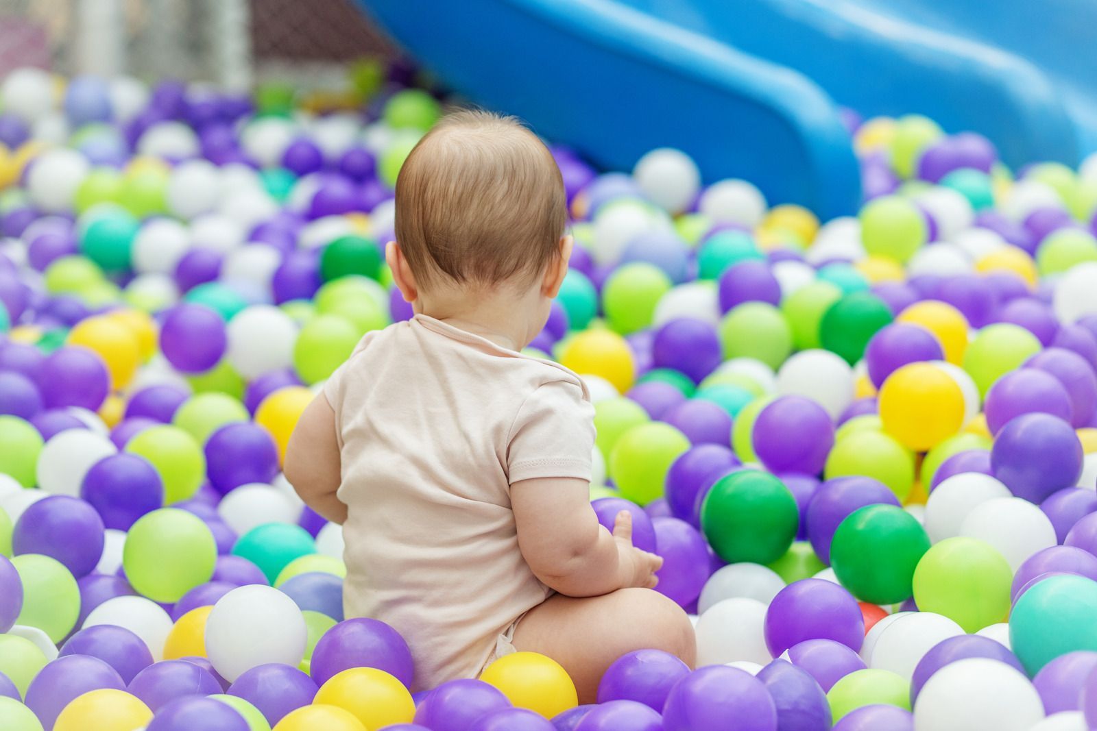 Baby sitting in a ball pit of colorful balls, with a blue slide in the background.
