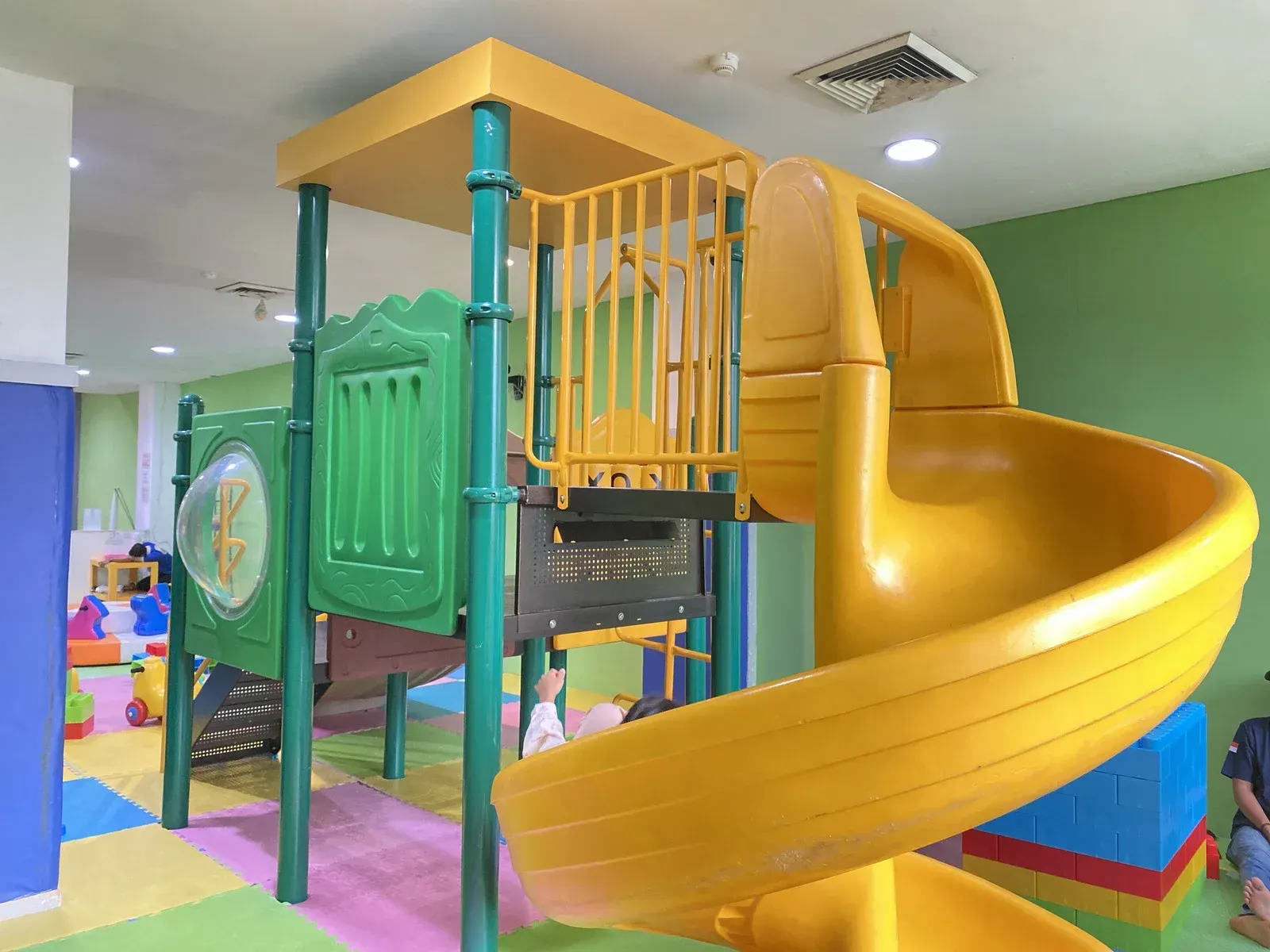 Indoor playground with yellow slide, green structure, and colorful floor mats.