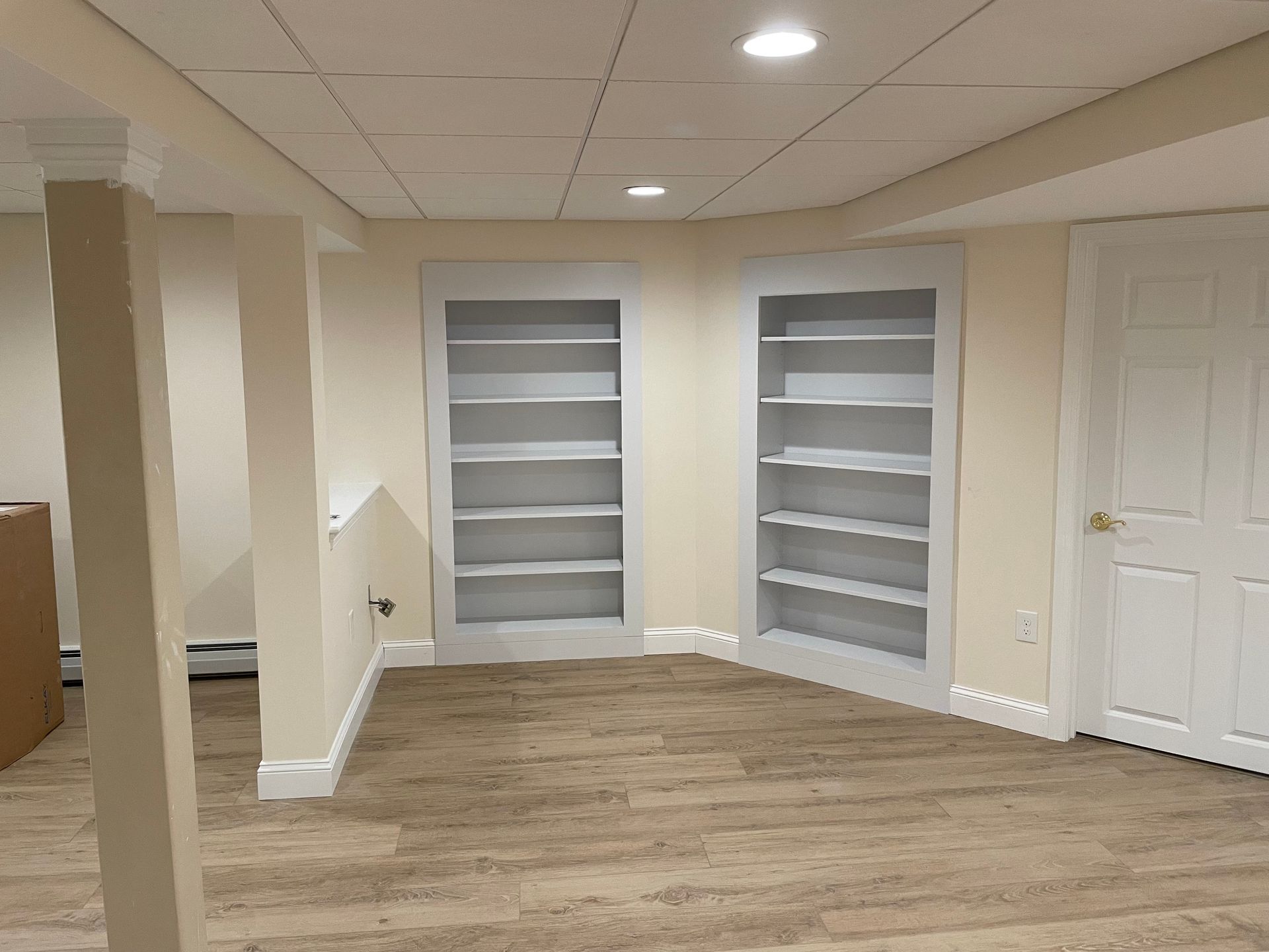 Empty room with two built-in bookshelves and a door, beige walls, carpet flooring.