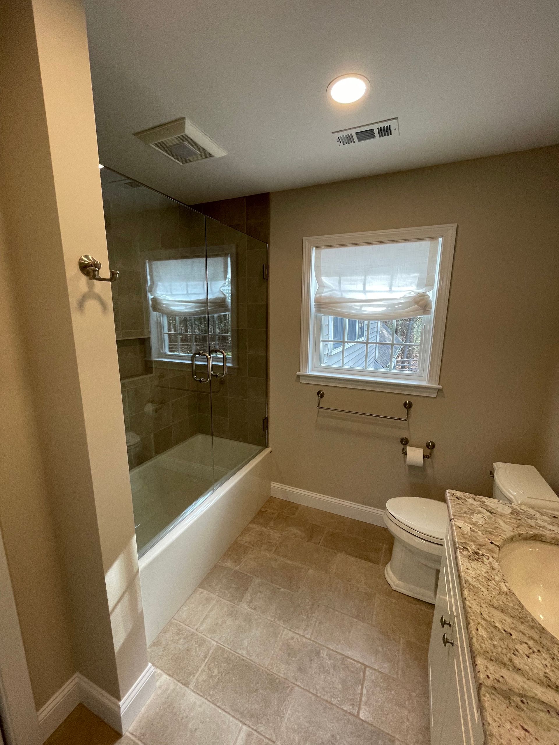 Bathroom with tub, toilet, and vanity. Beige tile and walls, window with blinds.