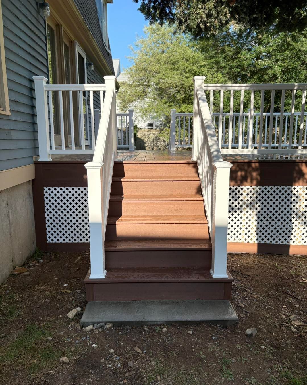 Wooden deck with white railing, stairs, and lattice skirting, attached to a blue house.