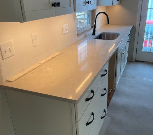 White kitchen cabinets with light countertops and a black faucet and handles.