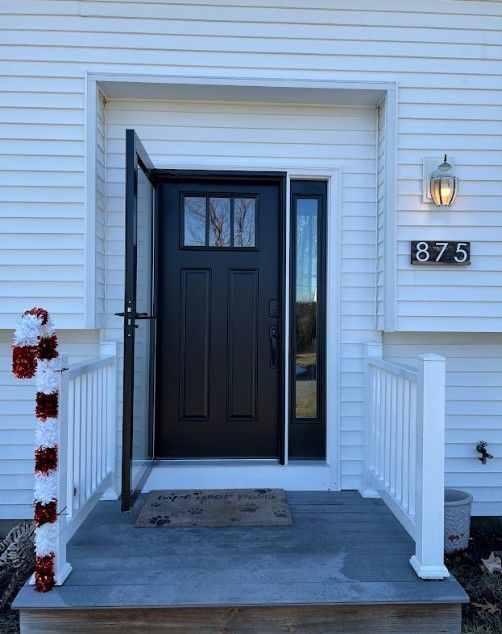 Black front door with sidelight and open screen door; white house with porch and address