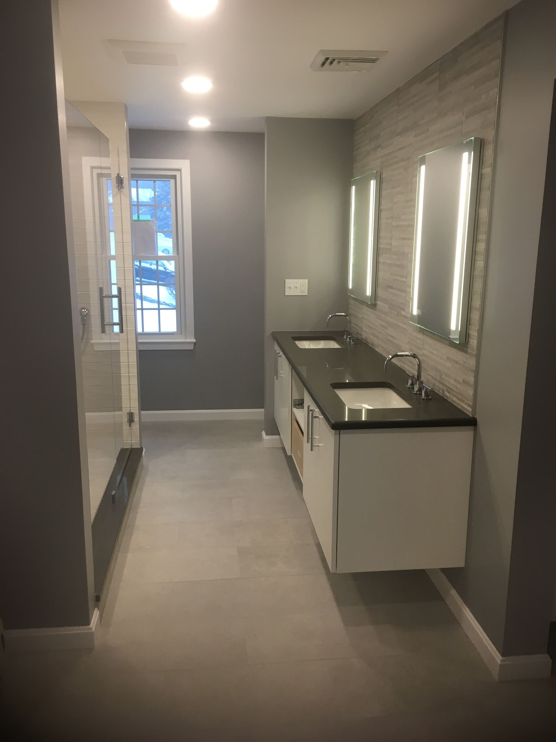 A bathroom with two sinks , a shower and a window.