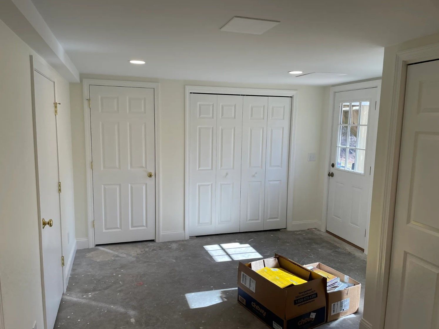 Interior of a room with white walls, doors, and a sliding closet. Boxes on the floor, unfinished concrete floor.