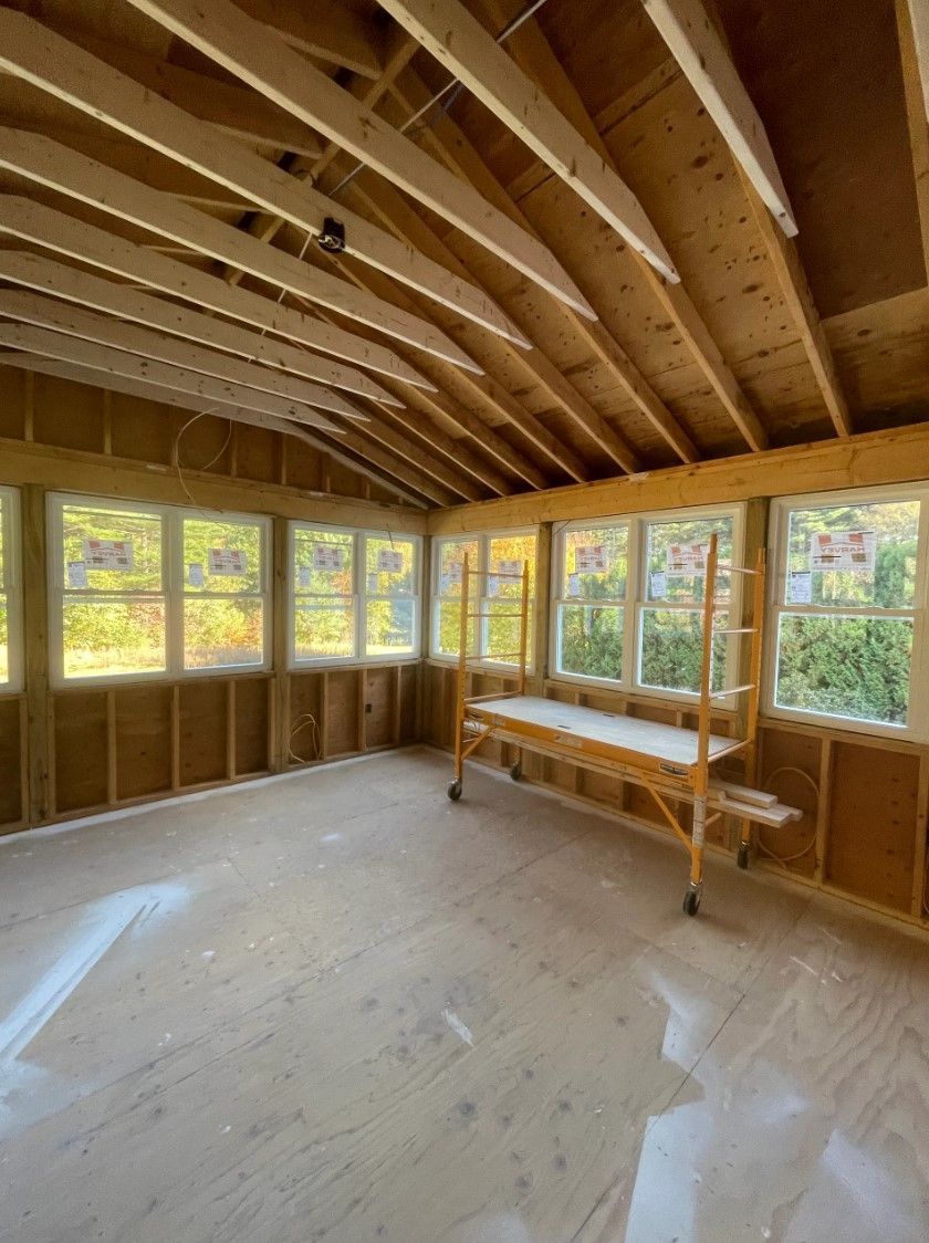 Interior view of a sunroom under construction, with wooden framework, windows, and scaffolding.